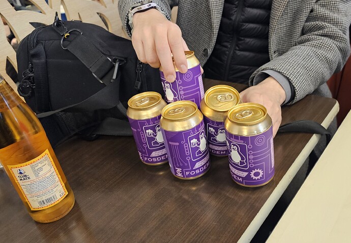 FOSDEM 맥주 4캔을 테이블 위에 늘어뜨린 모습.